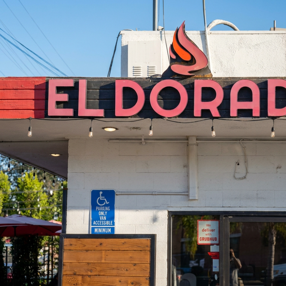 Exterior of El Dorado restaurant with red signage, flame logo, shaded patio, flowering plants, and accessible parking sign.